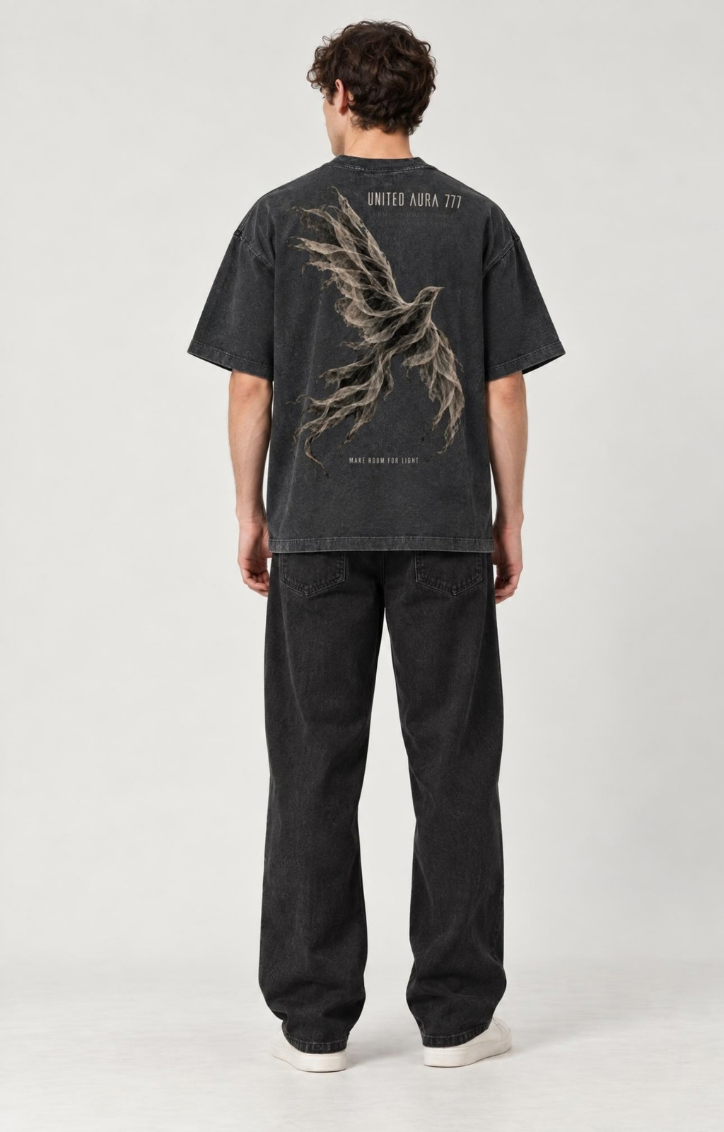 A model viewed from the back wearing a faded black graphic t-shirt with a large bird design and 'UNLAWFUL ARK' text, paired with dark jeans and white sneakers, against a plain light gray background.