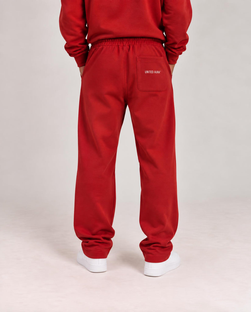 A person shown from the back wearing red sweatpants with a small white 'UNITED ARMY' logo on the back pocket, paired with a matching red sweatshirt and white sneakers, against a light gray studio background.