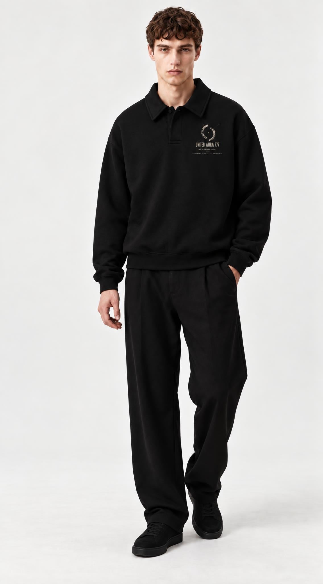 A man modeling a black long-sleeve polo sweatshirt and matching black sweatpants against a light gray studio background. The sweatshirt features a small circular logo and text on the left chest in a light beige color.