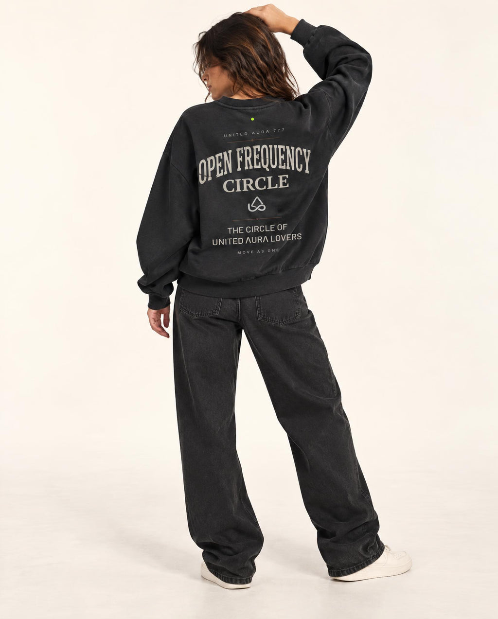 A model shown from the back wearing a black crewneck sweatshirt with 'OPEN FREQUENCY CIRCLE' printed in white on the back, paired with black jeans and white sneakers, against a plain white studio background.
