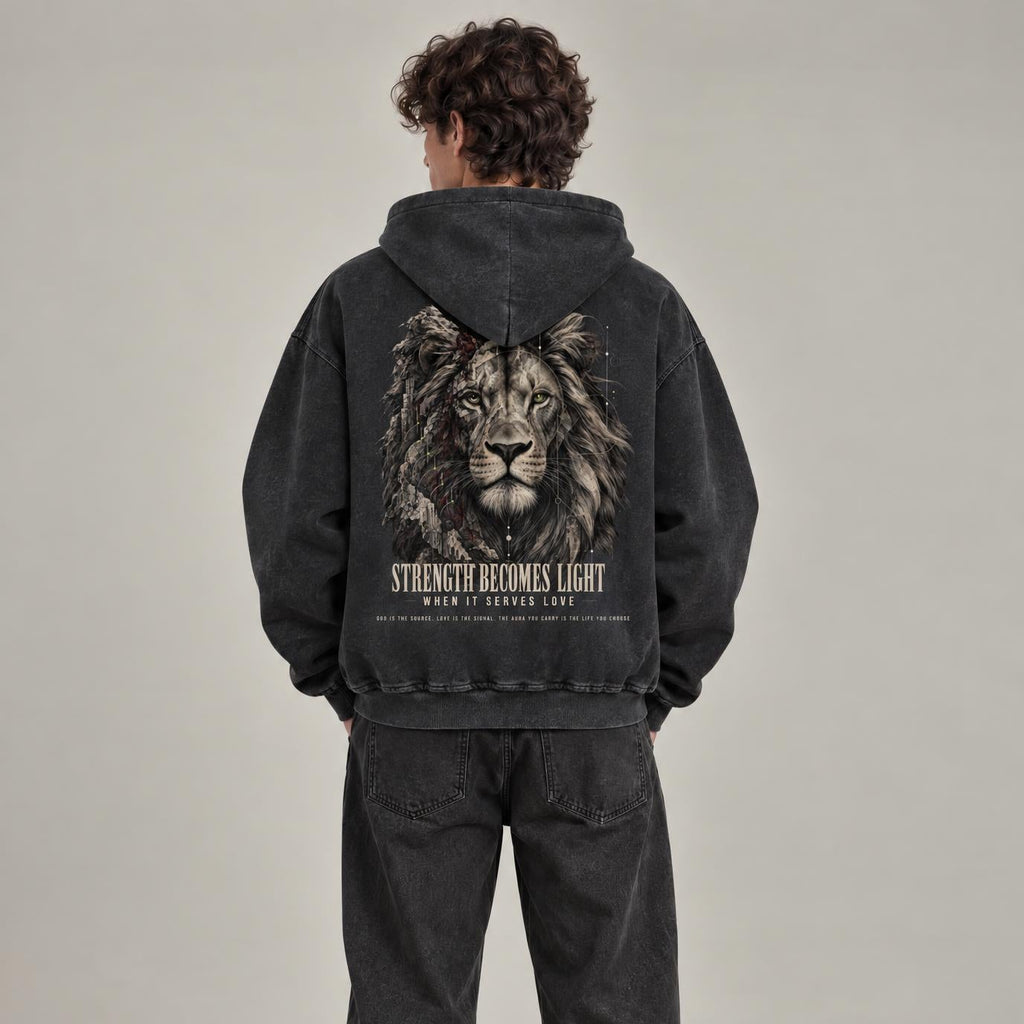 A model viewed from behind wearing a washed black hoodie with a large graphic of a lion on the back and the text 'STRENGTH BECOMES LIGHT' below it, paired with matching washed black sweatpants and white sneakers, against a neutral studio background.