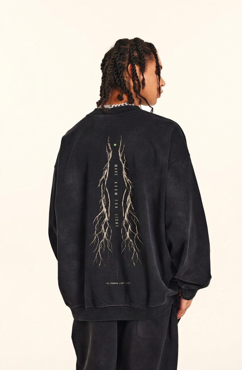 A person shown from the back wearing a faded black crewneck sweatshirt with a large white root-system graphic and text on the back, paired with black pants, against a plain off-white background.