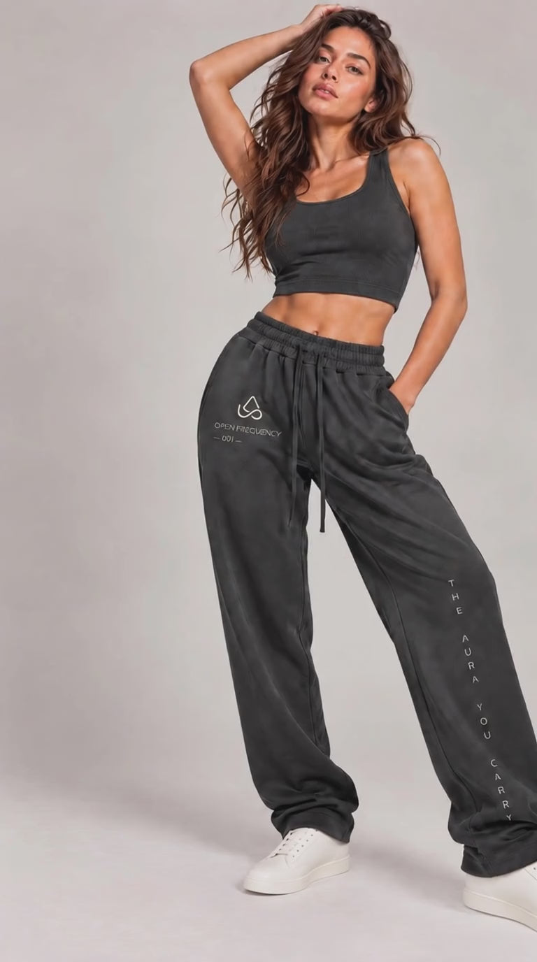video of  A woman modeling a dark gray two-piece activewear set consisting of a cropped tank top and matching jogger sweatpants, paired with white sneakers, against a neutral studio background.